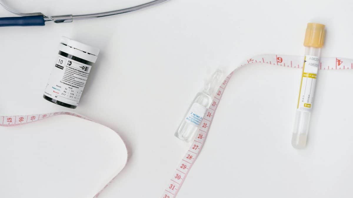 Collection of medical supplies including ampoules, vials, and measuring tape on white surface.