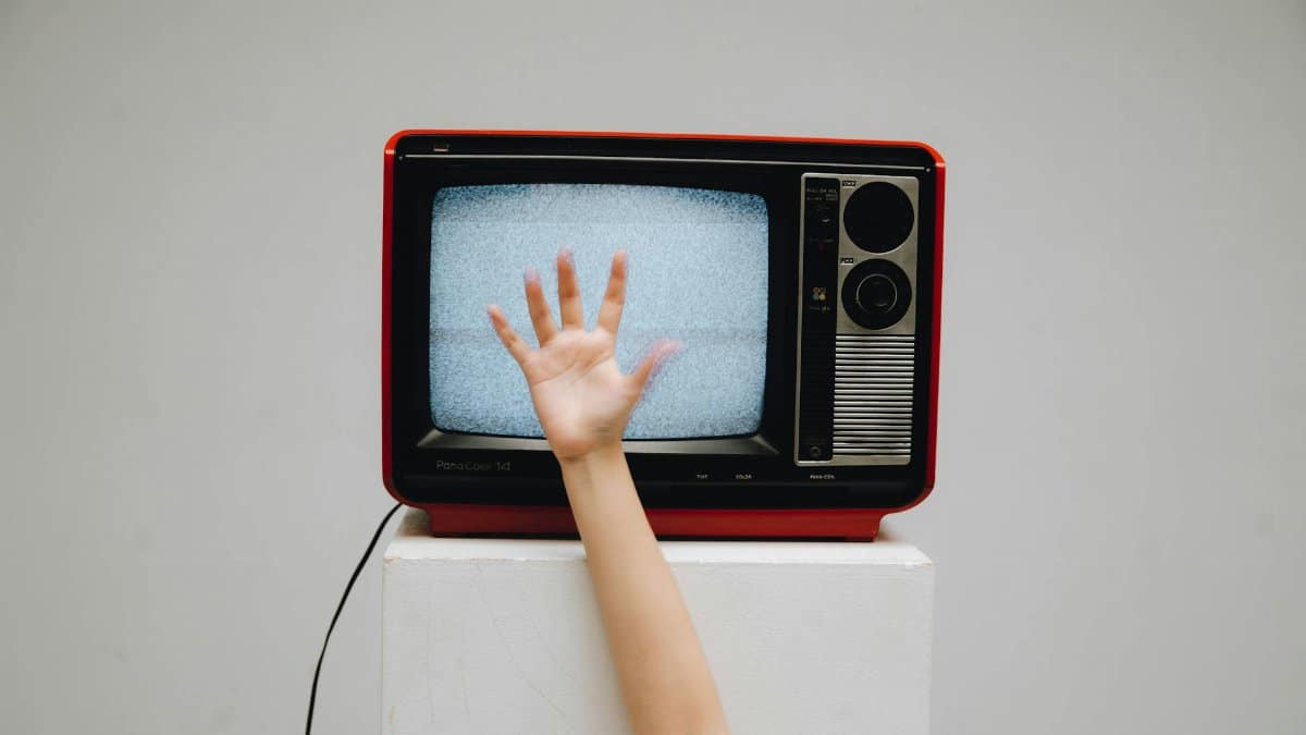 A classic retro television displaying static with a hand reaching towards the screen.