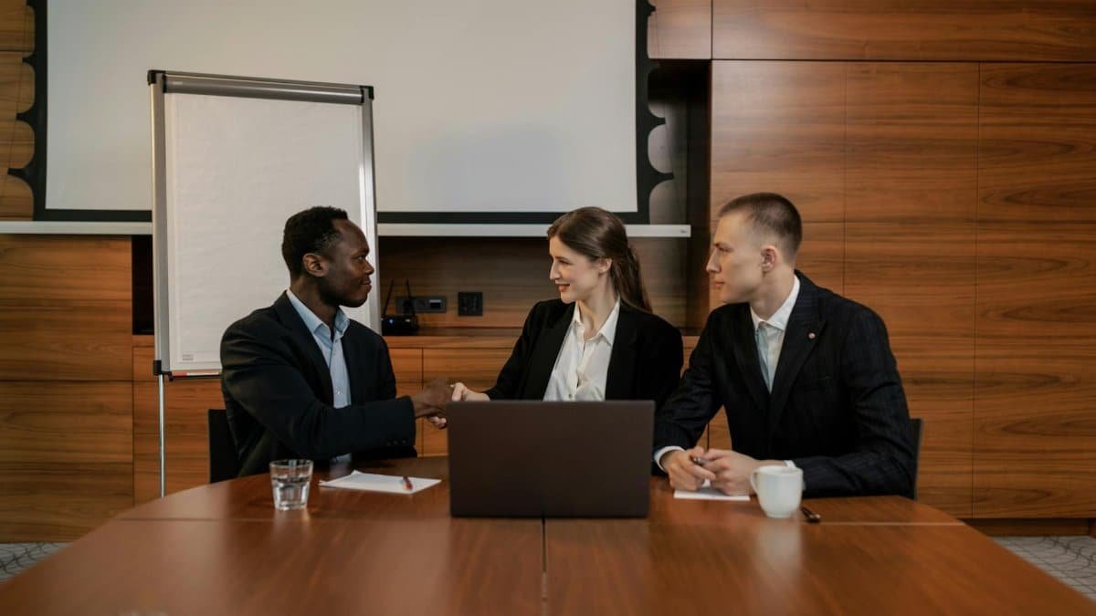 A diverse group of professionals engaged in a business meeting, collaborating and shaking hands in an office setting.