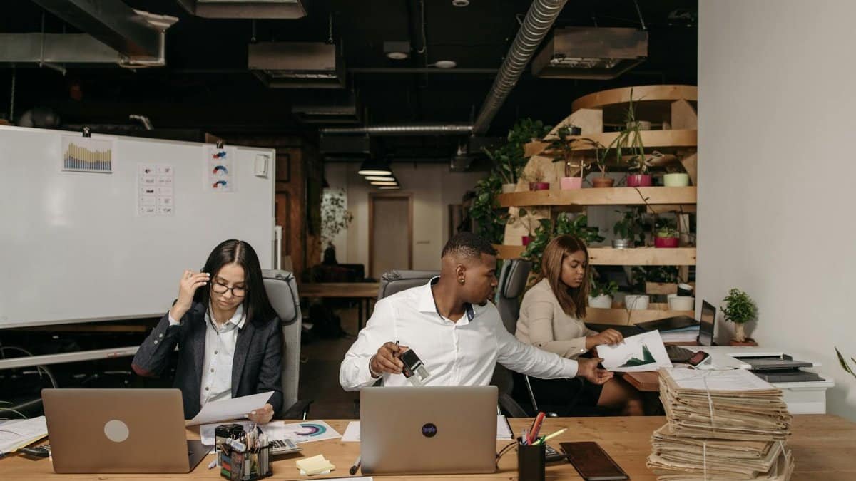 Diverse team collaborating in a modern office setting with laptops and documents.