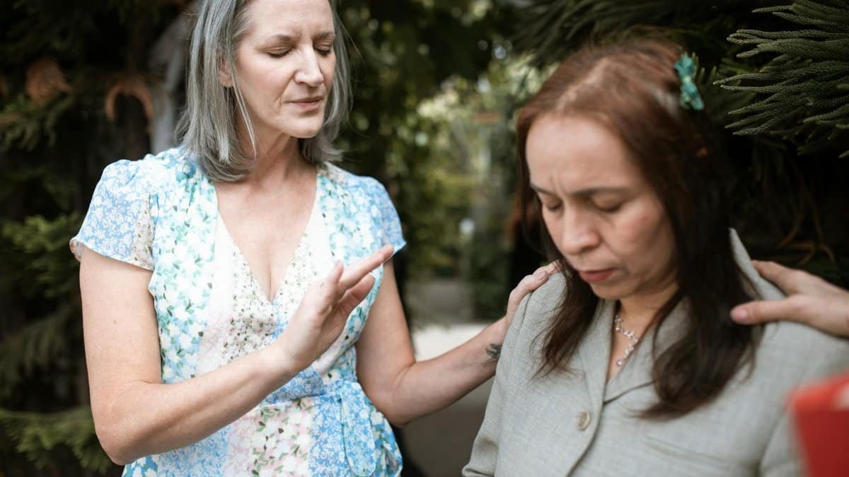 Two women in a peaceful prayer moment, sharing spiritual connection outdoors.