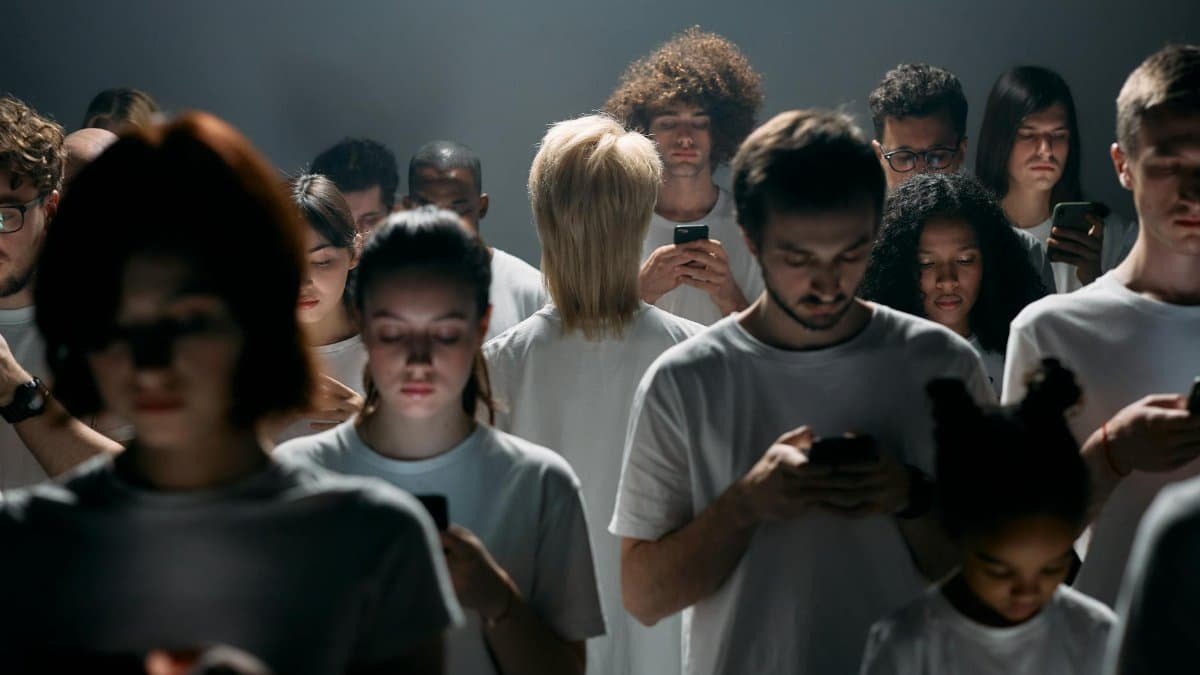 A large group of diverse individuals engrossed in smartphones, conveying themes of social isolation and digital future.