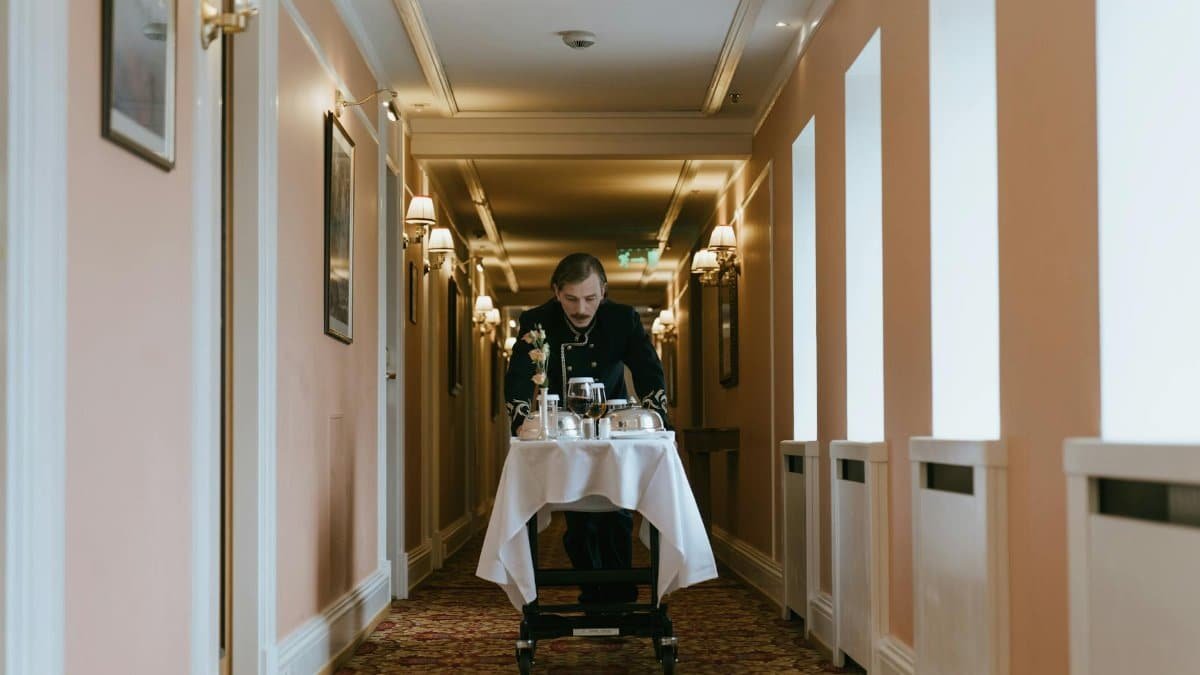 A hotel staff member pushes a room service trolley in a luxurious corridor.