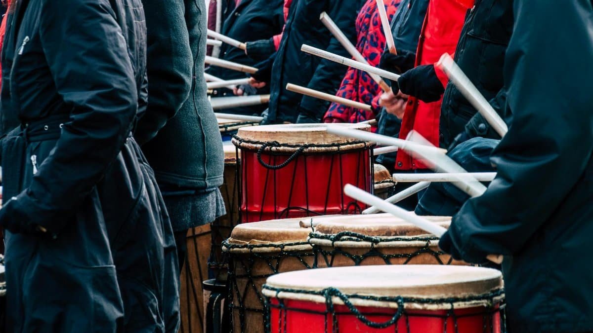 A group of people playing traditional red taiko drums outdoors in winter.