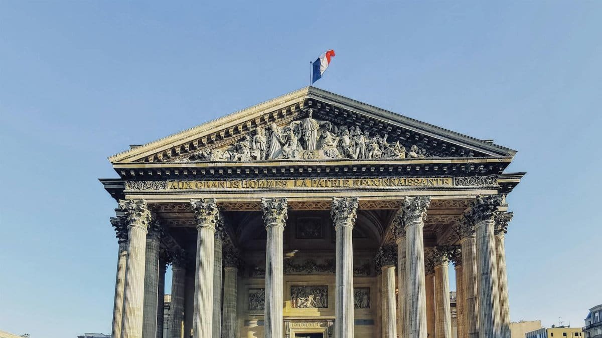 Front view of the Panthéon in Paris, featuring its iconic columns and French flag under a clear blue sky.