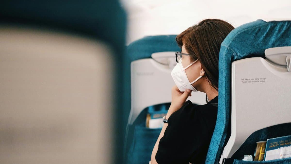 A woman sits on an airplane, wearing a face mask during the flight, representing the new normal of air travel.