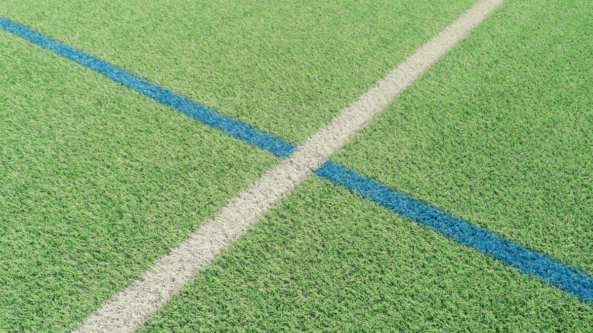 Close-up of intersecting white and blue lines on a vibrant green sports field grass surface.