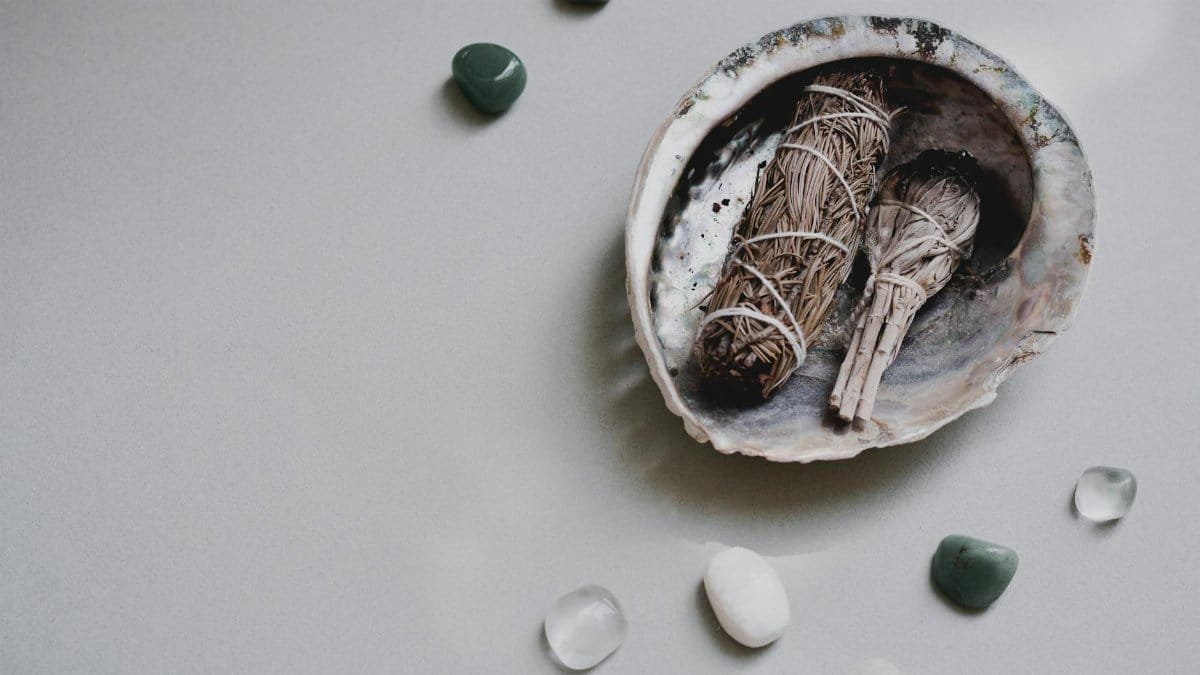 Flat lay of sage bundles and gemstones in an abalone shell for spiritual rituals.