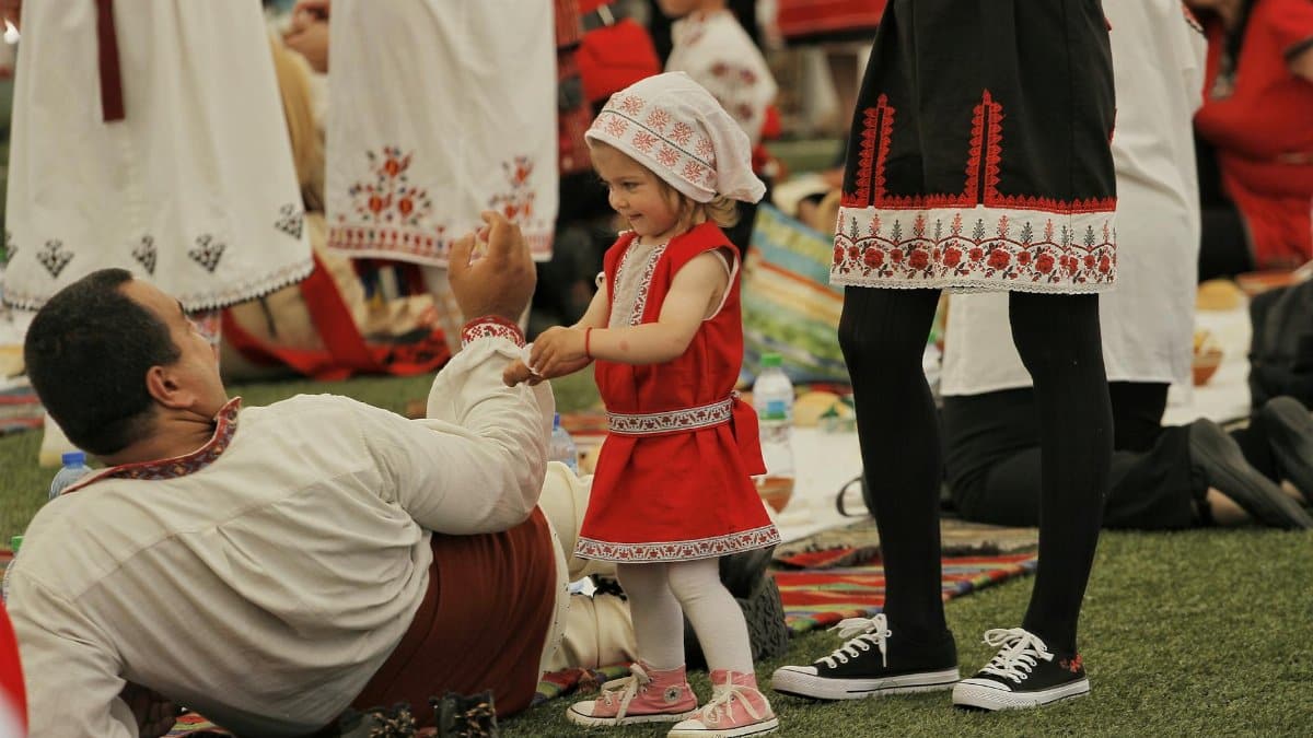 Child in vibrant traditional attire enjoying cultural festival outdoors.