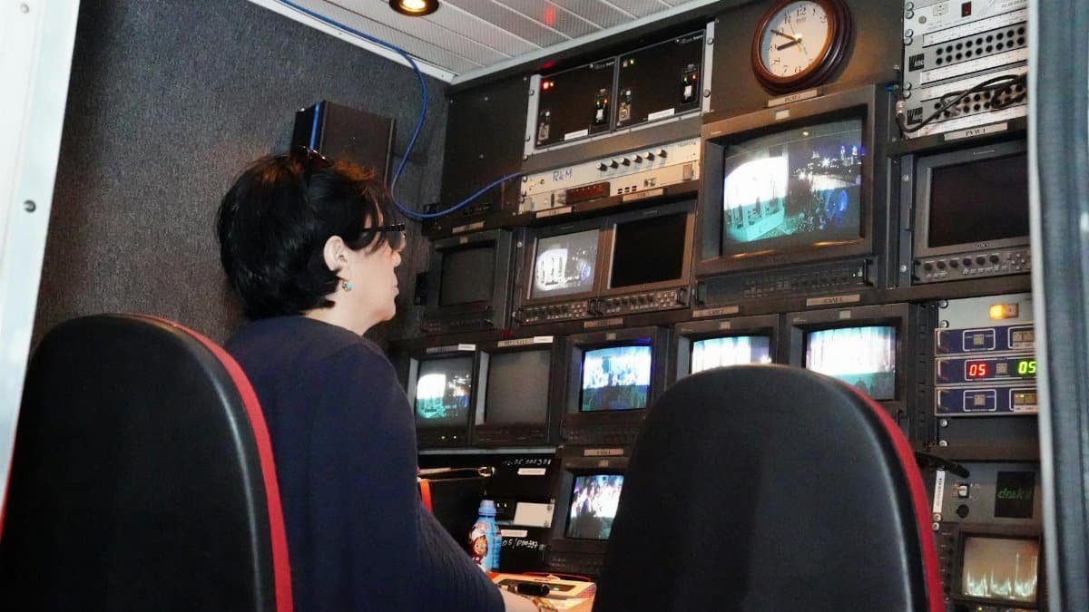 A professional in a TV broadcast control room with multiple screens and equipment.