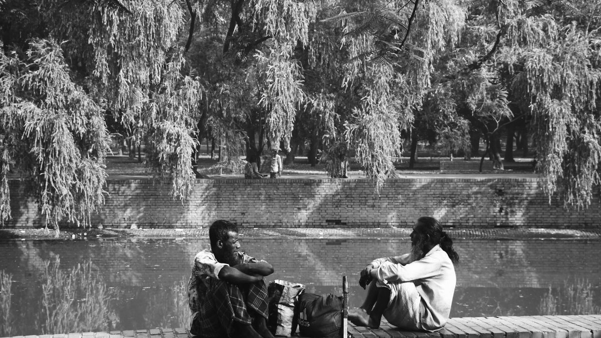 Two men engaged in conversation by a pond in Dhaka, capturing a moment of connection.