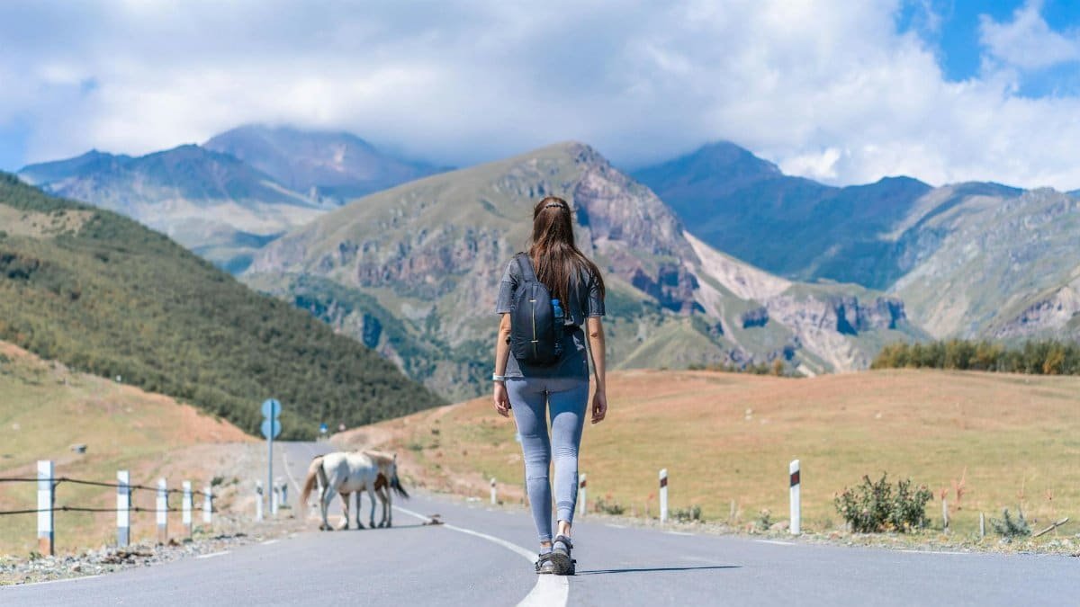 Back view of woman with backpack walking on road in Stepantsminda, Georgia's stunning mountains.