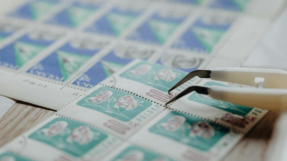 Vintage postage stamps with tweezers on a desk, ideal for collectors and philatelists.