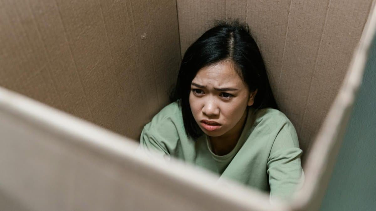 A woman inside a cardboard box showing a distressed expression, symbolizing anxiety or claustrophobia.