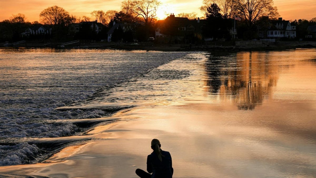 Silhouette of person sitting by the water at sunrise in Cove Island Park, Stamford.