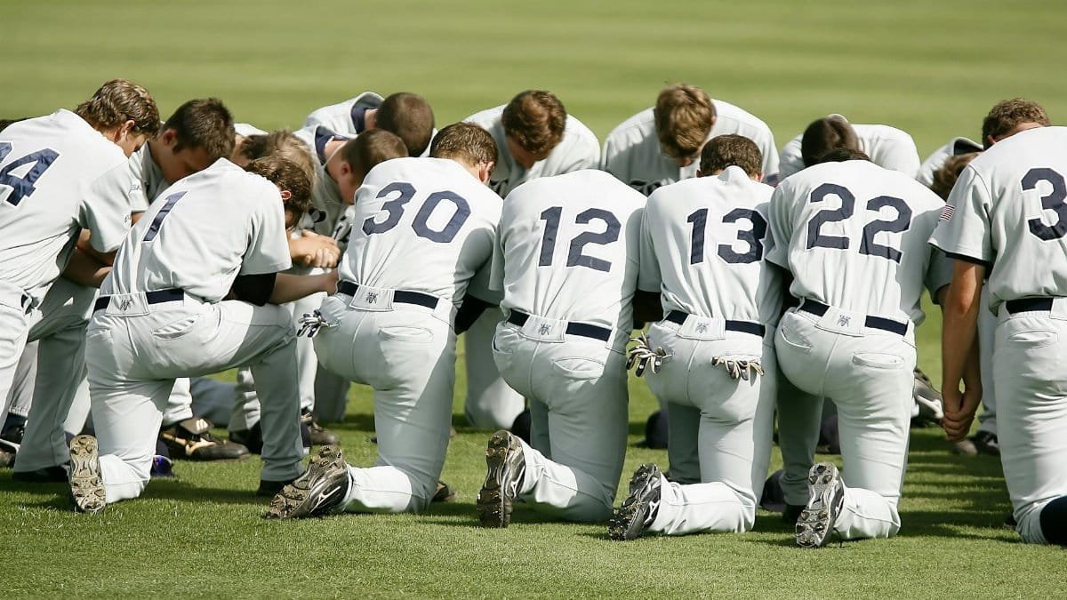Group of baseball players in uniforms kneeling together on a sports field.