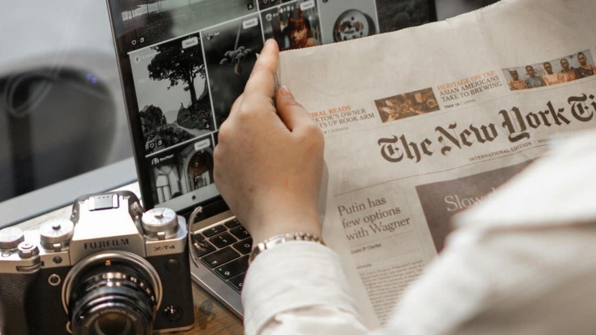 Close-up of a person reading The New York Times by a laptop and camera.