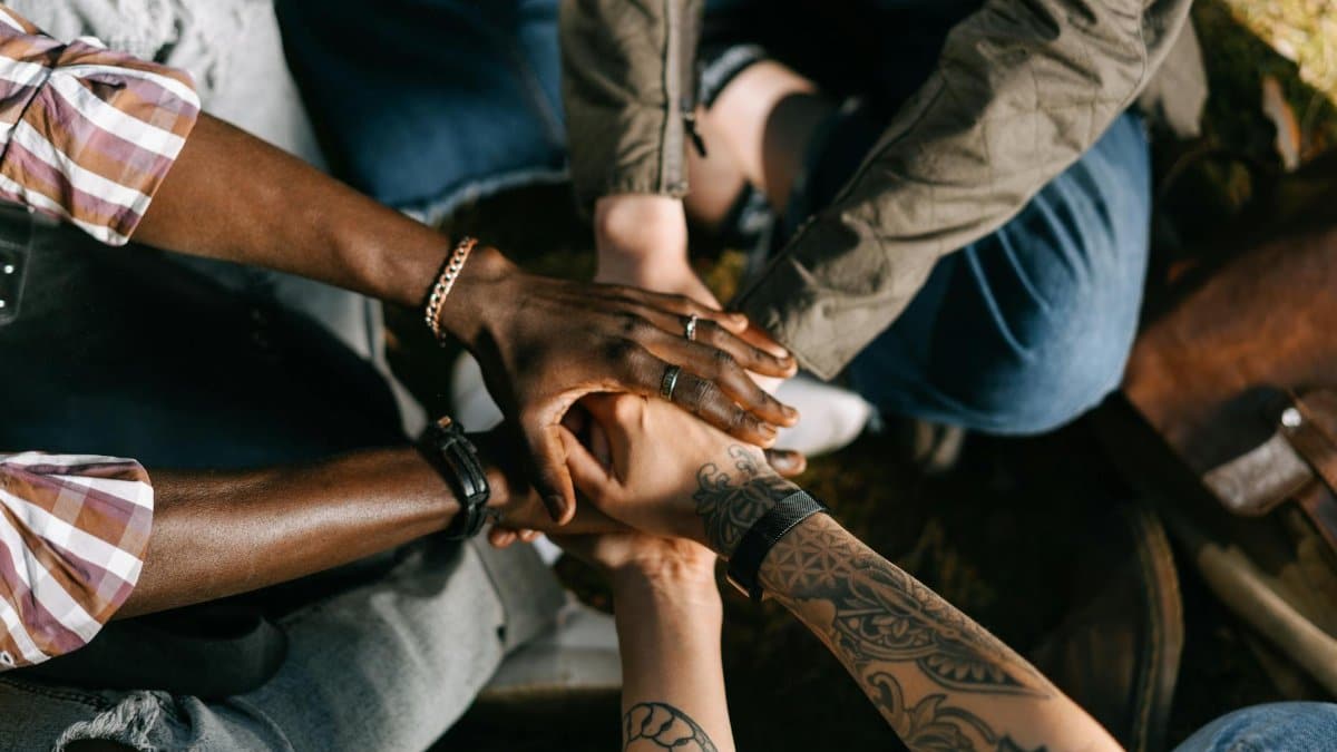A diverse group of individuals uniting in solidarity with hands stacked together outdoors.