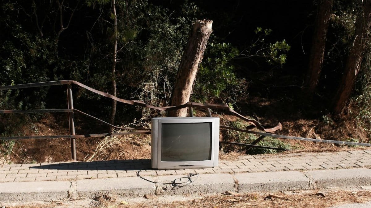 An abandoned tube television on a sidewalk surrounded by nature in Izmir, Türkiye.