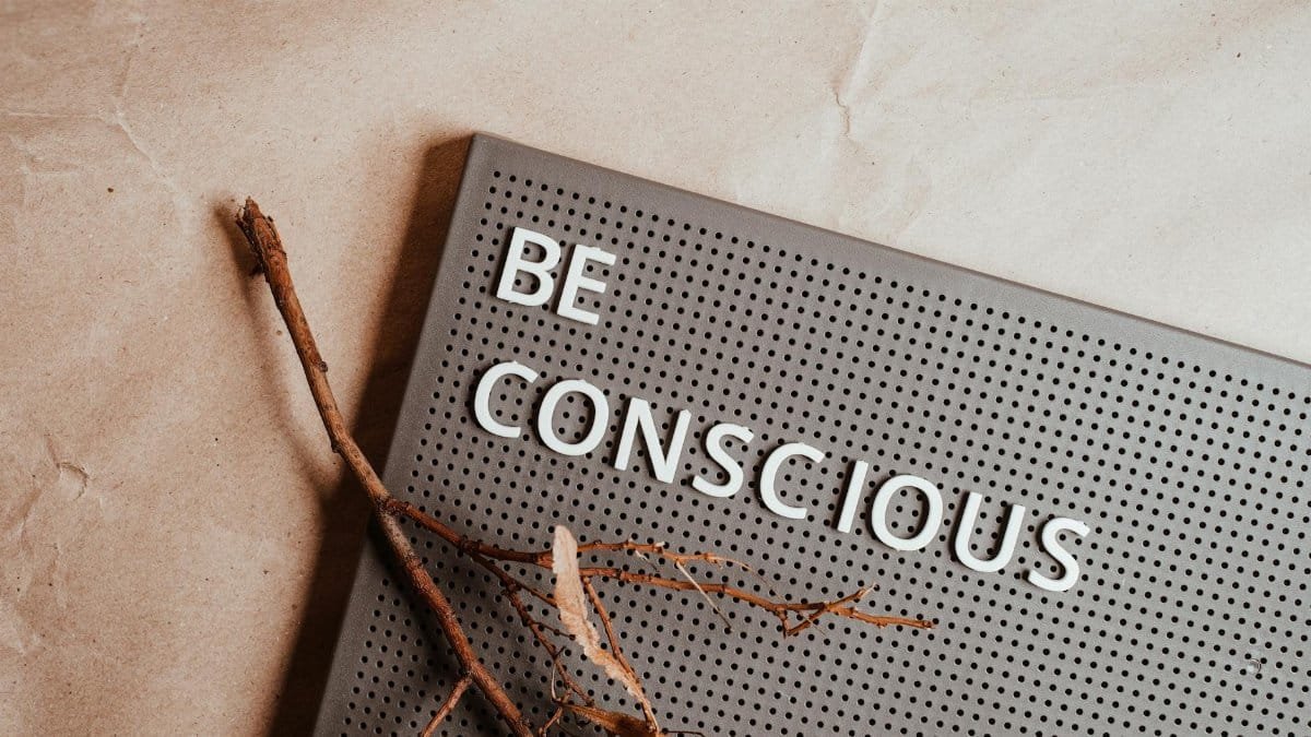 A flat lay of a pin board with the phrase 'Be Conscious' and natural elements.