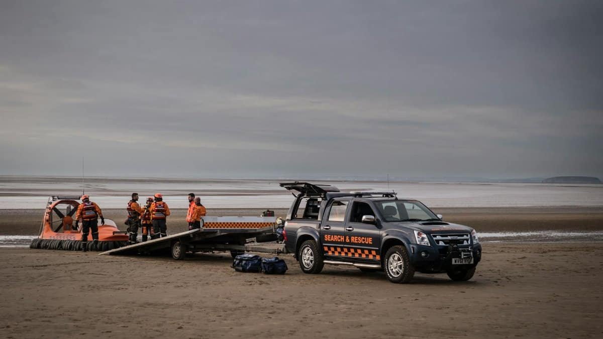 Search and rescue team with hovercraft and vehicle on a coastal mission.