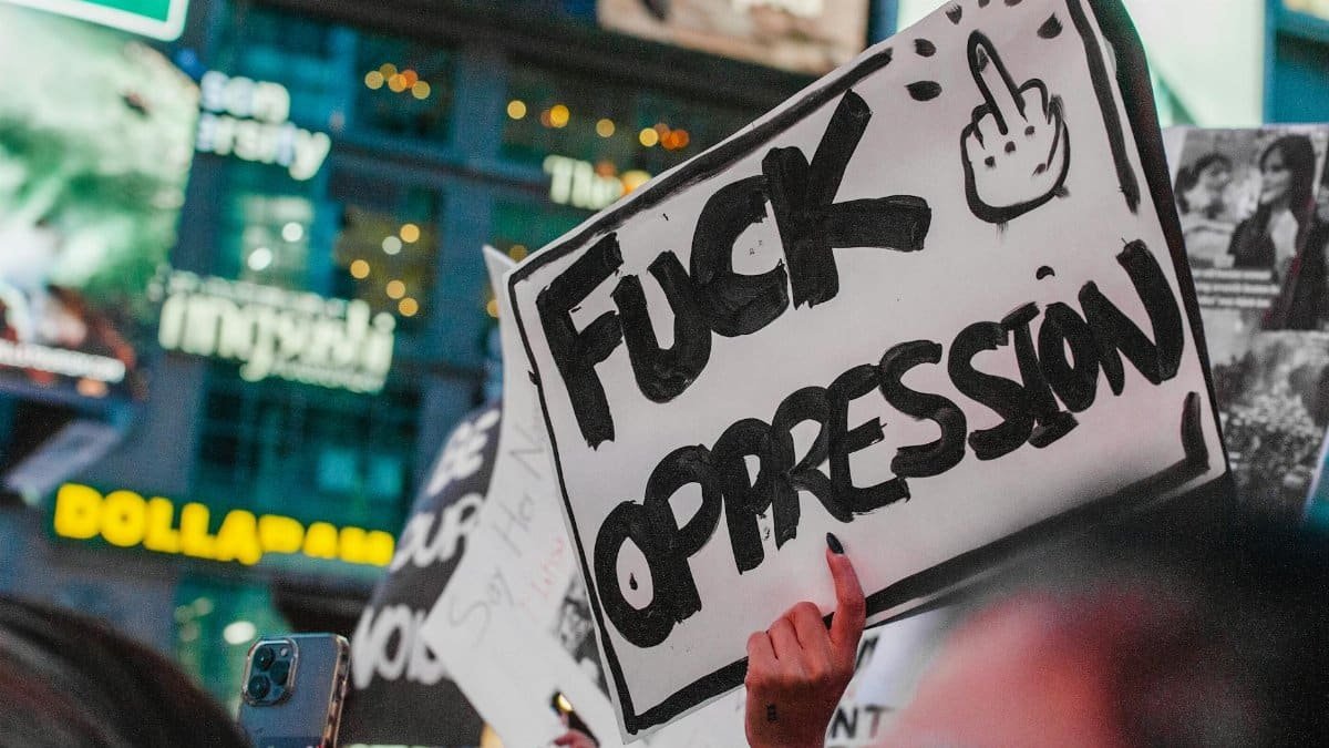 Protesters holding a bold sign against oppression in a lively city scene.