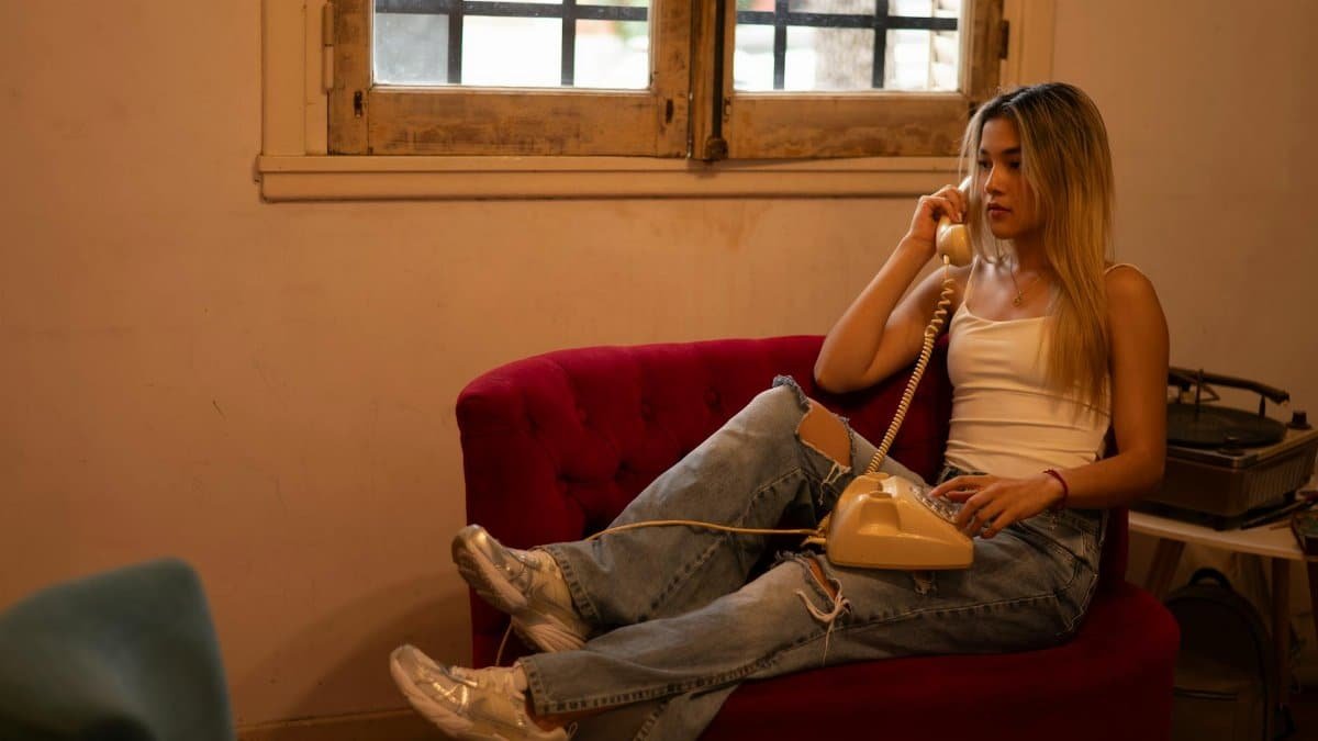 Casual scene of a young woman in a white tank top using a vintage rotary phone indoors.
