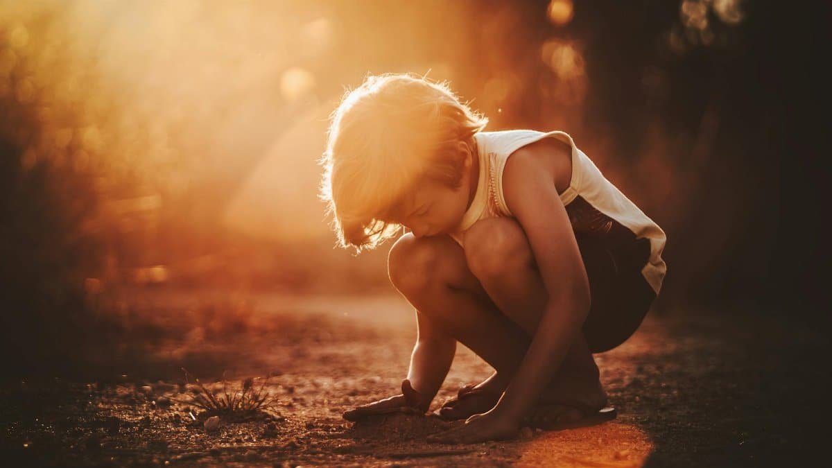 Full body of child in casual clothes squatting and playing with sand in park
