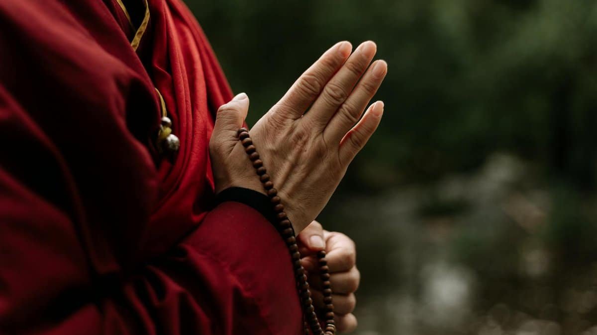 Close-up of monk in red robe meditating with prayer beads outdoors.