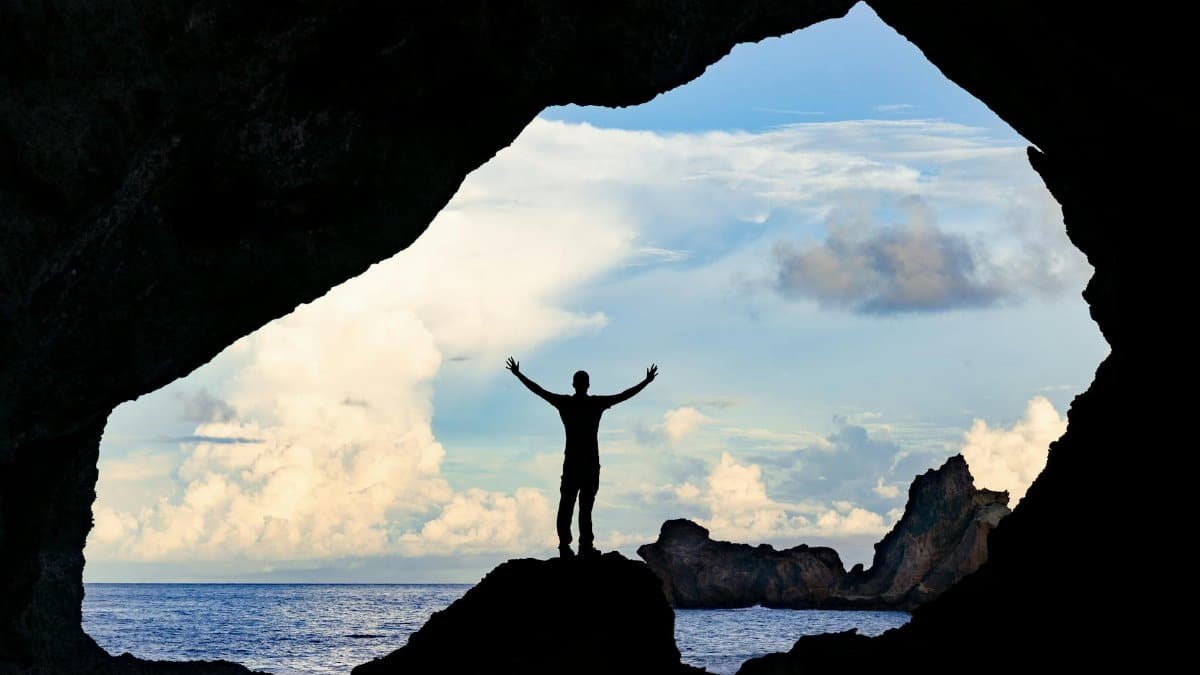 A person stands triumphantly in a cave in Taiwan overlooking the ocean, embracing exploration.