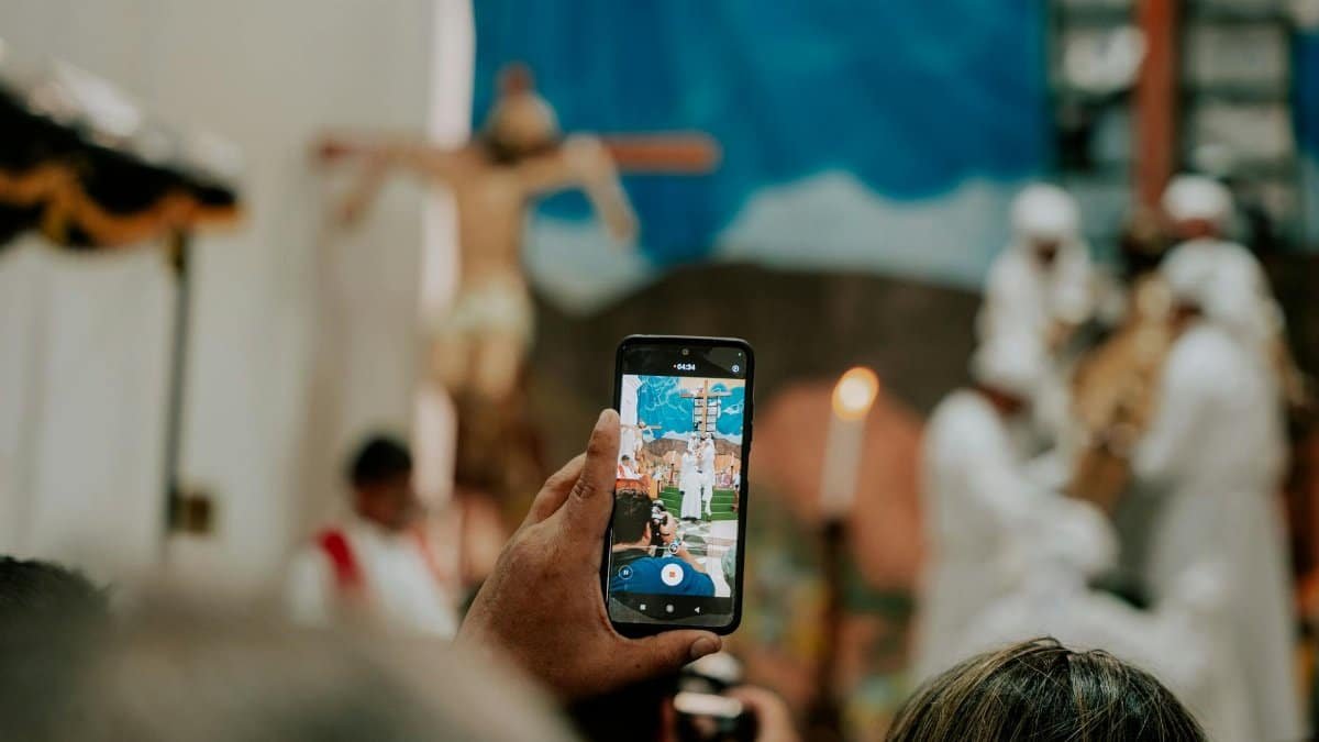 A person records a spiritual ceremony with a smartphone, focusing on religious symbolism and community.