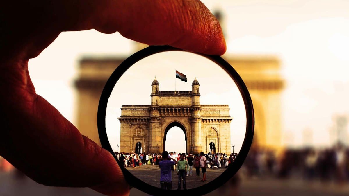 Artistic view of the Gateway of India through a camera lens filter with vibrant colors and bustling crowd.