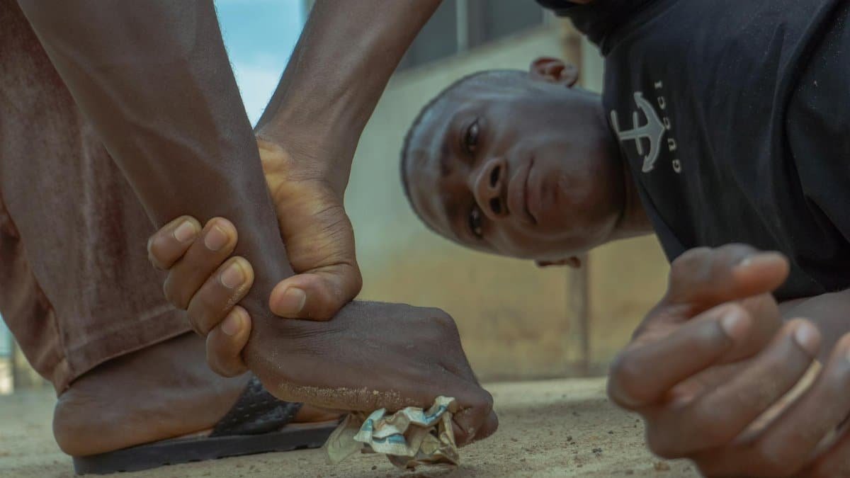A close-up shot of a person grasping a foot on a sandy ground, depicting struggle.