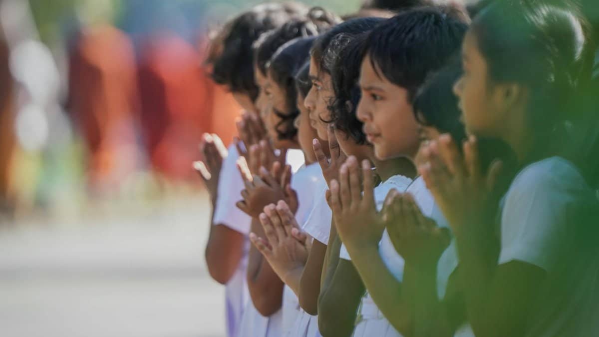 A group of school children in white uniforms participate in a religious procession, hands folded in prayer.