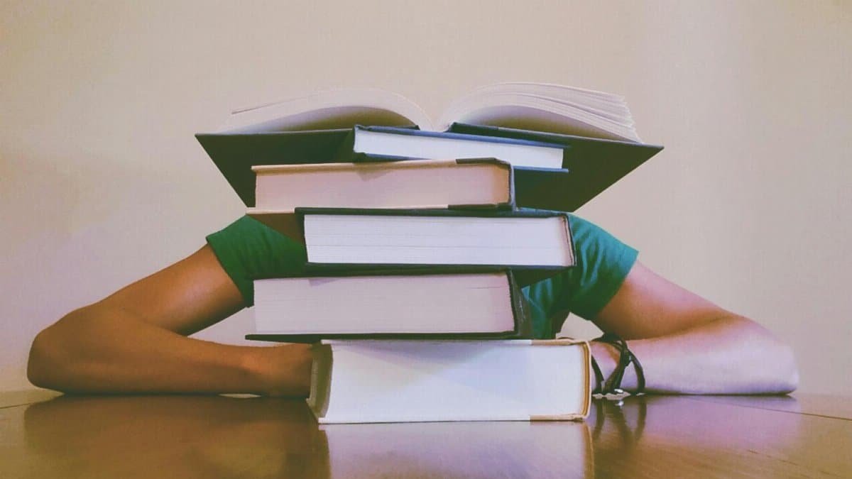 A student hidden behind a stack of books, symbolizing academic stress and study challenges.