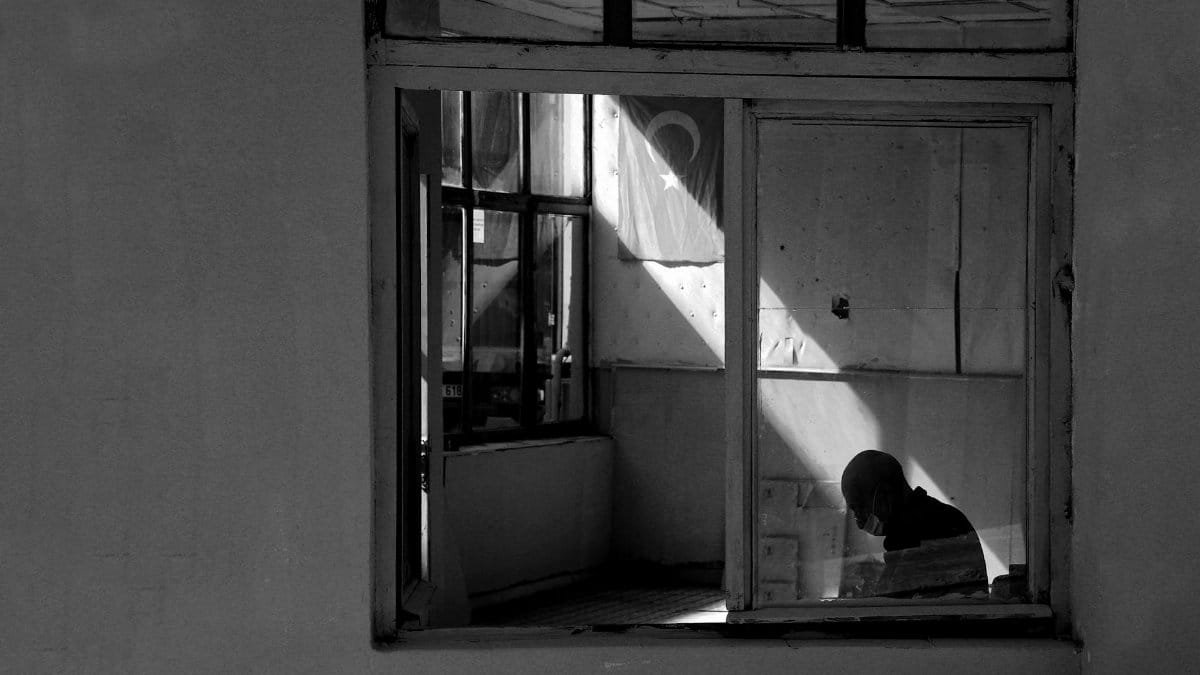 Black and white photo of a person indoors, with a Turkish flag visible through the window.