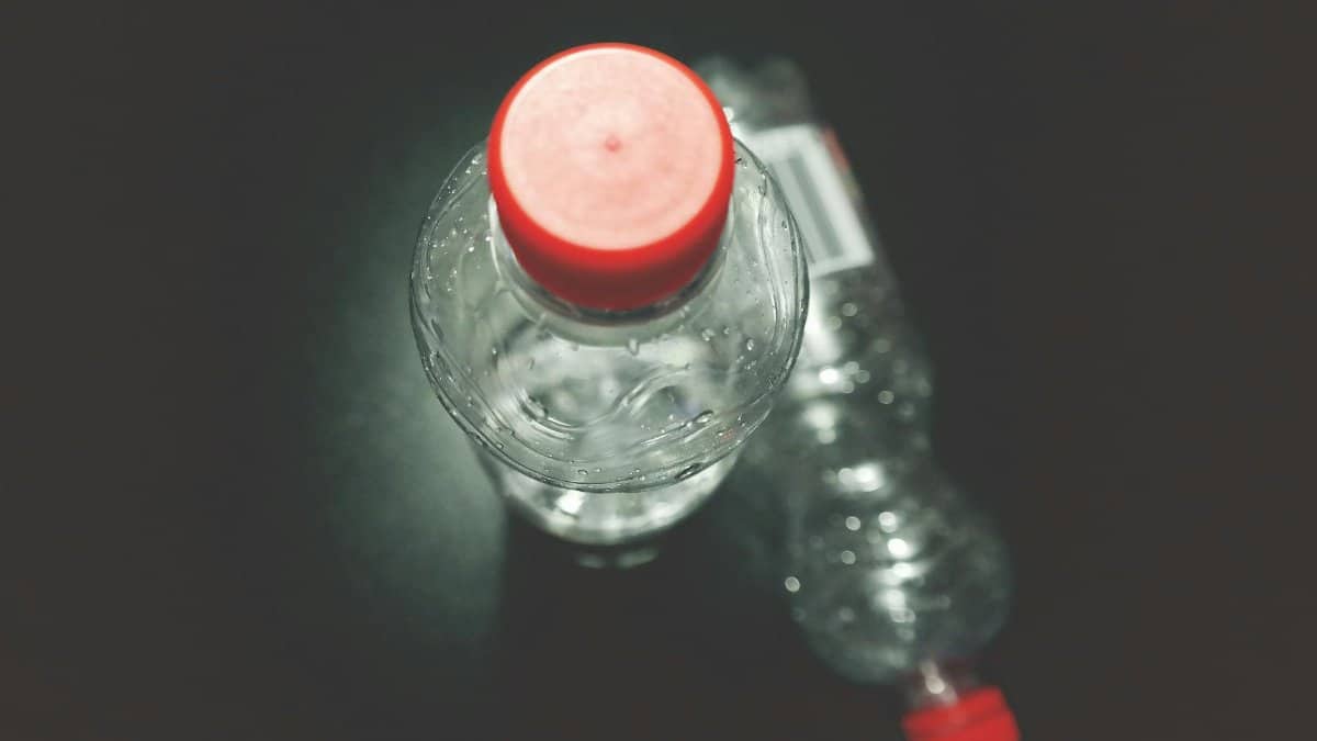 Top view of two clear plastic bottles with red caps on a dark surface, highlighting recycling.