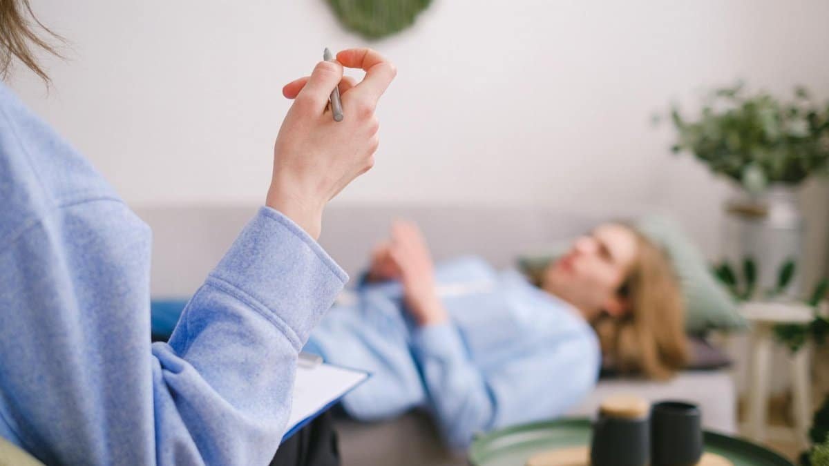 Therapist taking notes during a therapy session with a relaxed client lying on a couch.