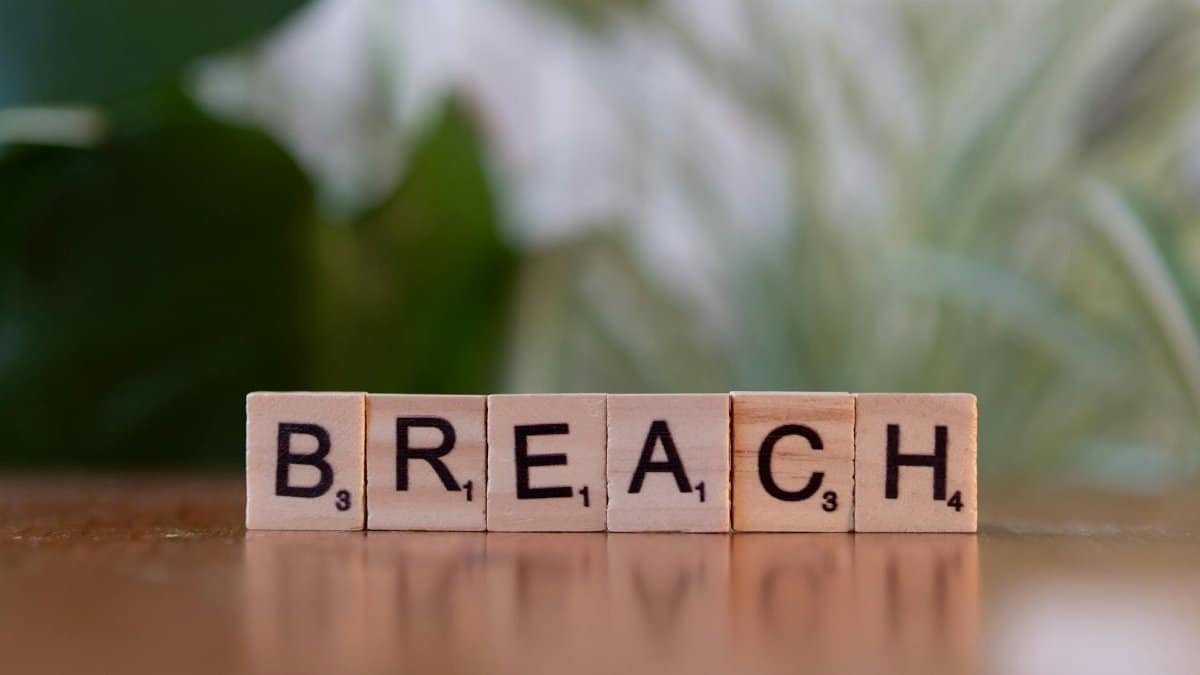Wooden letter tiles spell 'Breach' against a blurred natural background, concept of security or violation.