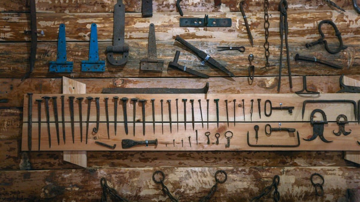 An array of vintage tools and nails displayed on a rustic wooden wall, showcasing craftsmanship history.