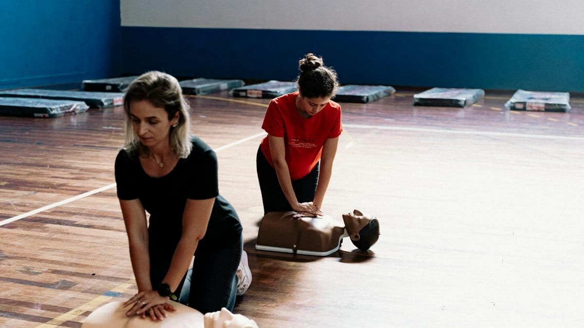 Two women learn CPR techniques on mannequins during a first aid training session.