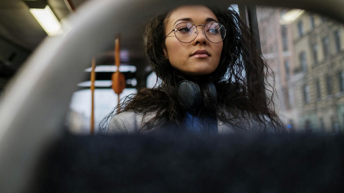 Portrait of an Asian woman with glasses and headphones riding a city bus.