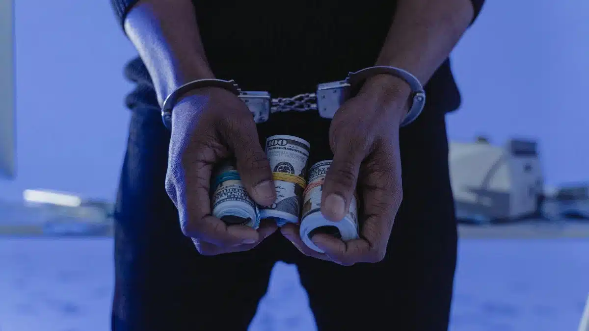 Close-up of handcuffed hands holding rolled cash, suggesting crime or arrest.