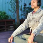 Adult man practicing meditation and relaxation with headphones in a serene outdoor setting.