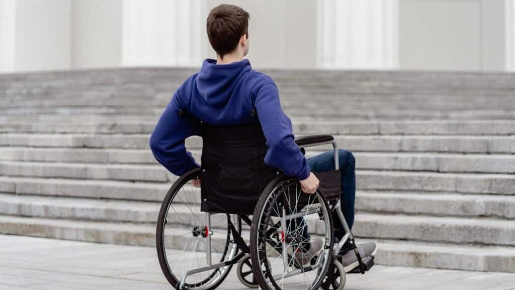 Back view of a young man in a wheelchair facing steps in a city setting.