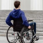 Back view of a young man in a wheelchair facing steps in a city setting.