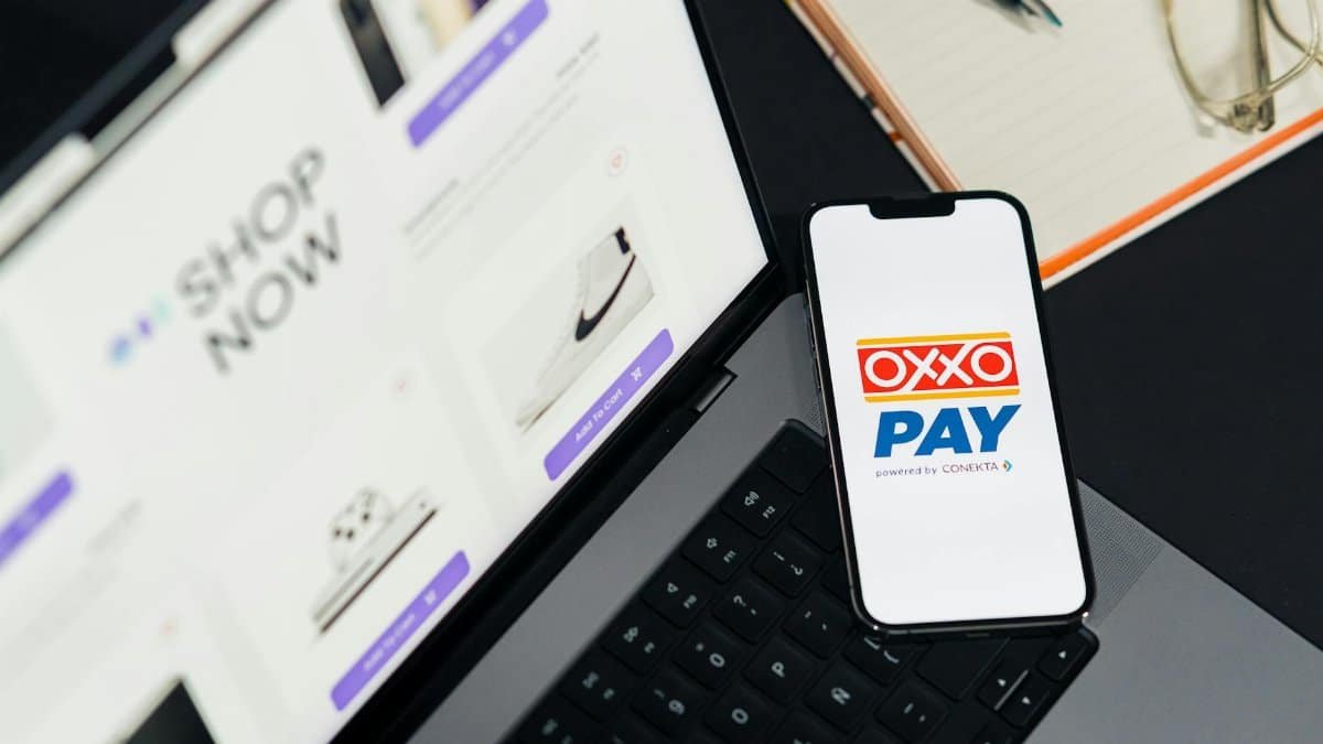 A mobile phone with OXXO Pay on a laptop used for online shopping.