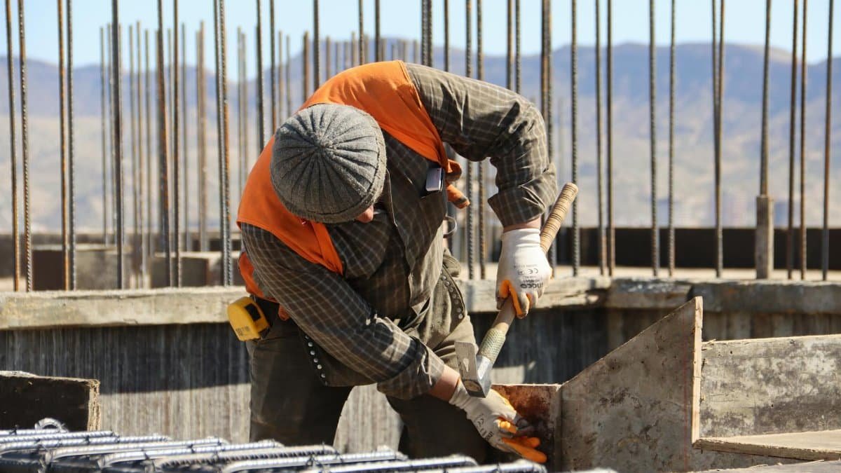 A construction worker in safety gear working at a sunlit site with mountains in background.