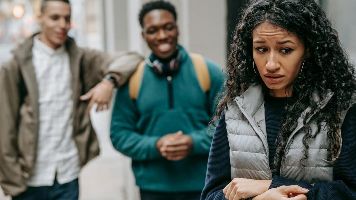 Laughing multiracial teenage boys mocking at depressed young ethnic female standing on street after school