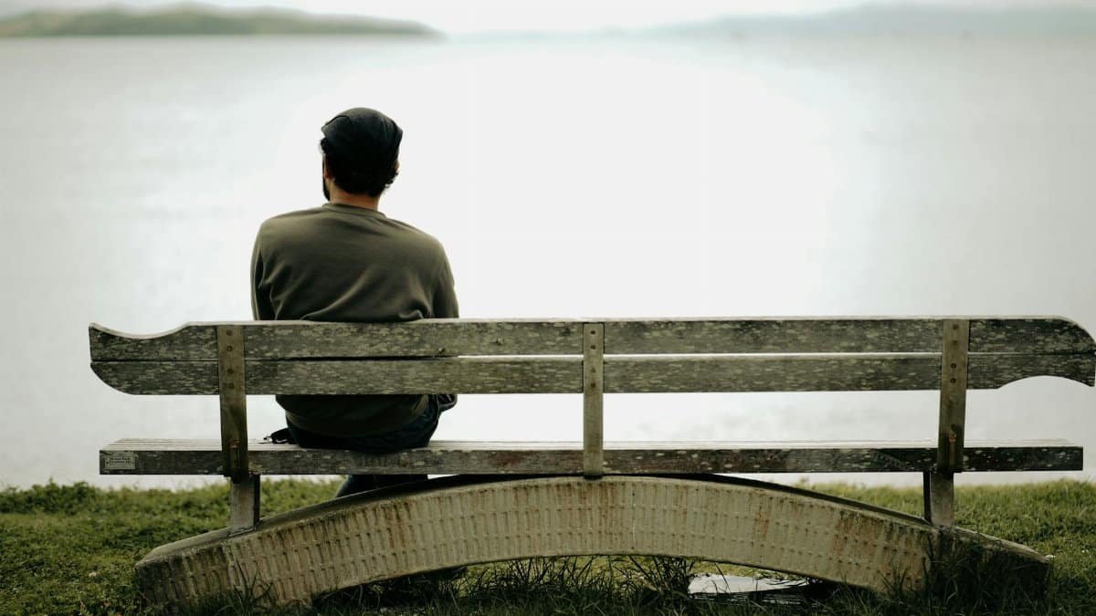 A person sits alone on a wooden bench by the water, capturing peaceful solitude.